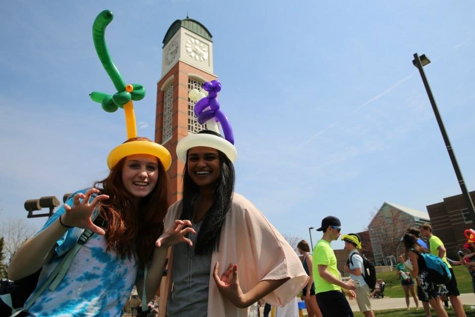 Two students wearing balloon hats in front of the clock tower